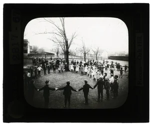 Foto horizontal en blanco y negro de niños y niñas tomados de la mano formando círculos al aire libre